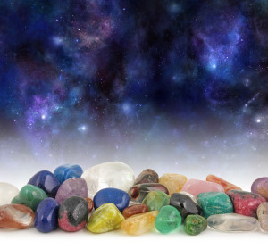 Cosmic Healing Crystals - Deep space background with stars, suns and planets with a selection of multicolored tumbled healing crystals at the front and plenty of copy space above